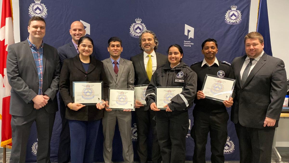 Photo of nine people standing in a row facing the camera, 5 of which are holding citations